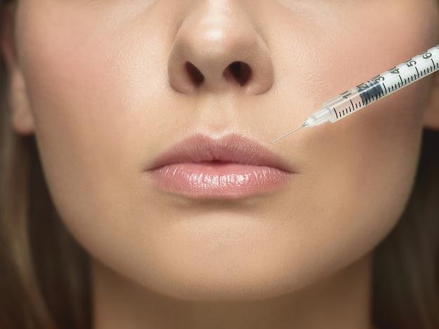 A close-up image of a woman's lower face receiving an injection in her lips, highlighting a cosmetic procedure for lip enhancement.