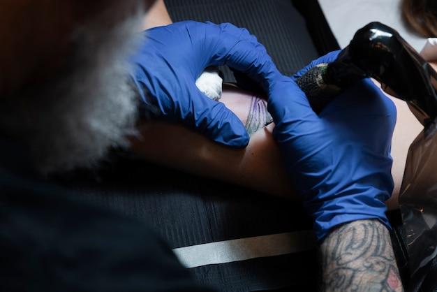 Tattoo artist working on a client's arm, wearing blue gloves, focus on tattooing process.