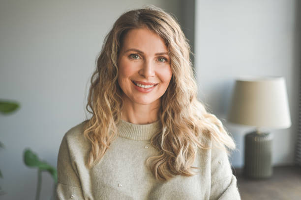 Smiling woman with blonde curly hair wearing a beige sweater in a cozy room