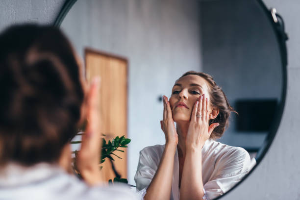 Woman applying skincare products while looking in the mirror