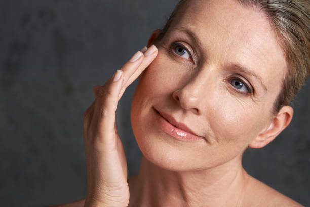 Mature woman with healthy skin touching her face gently against a dark background