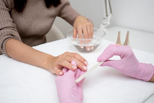 Manicure in progress at a nail salon with a client's hand being treated by a technician wearing pink gloves.